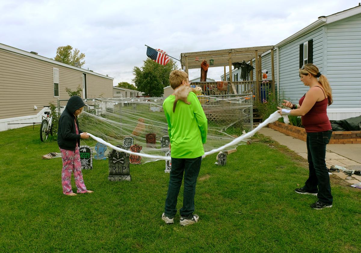 two young children hang Halloween decorations with their mother outside their mobile home