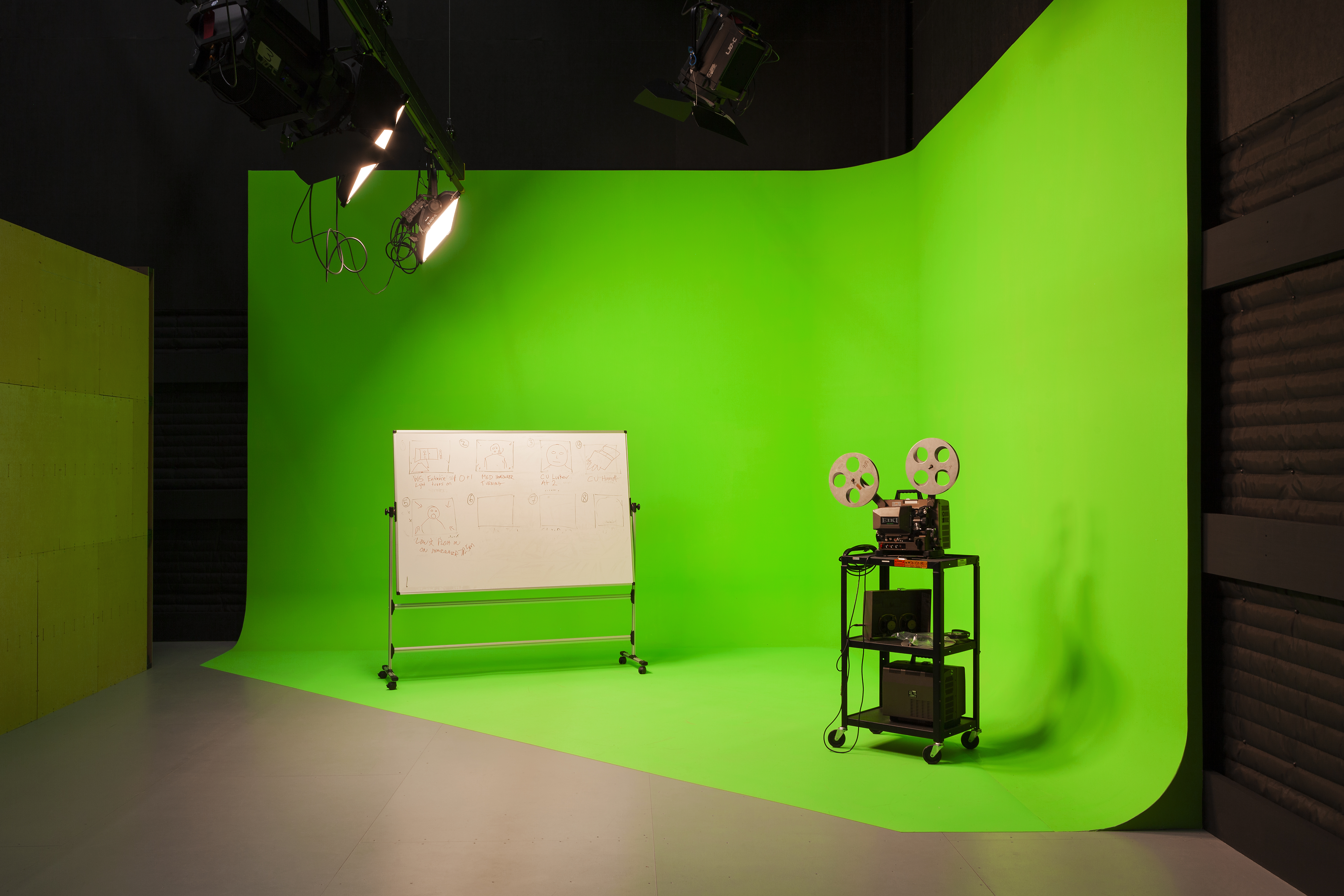 A white board and projector stand sitting on a green screen in a studio.