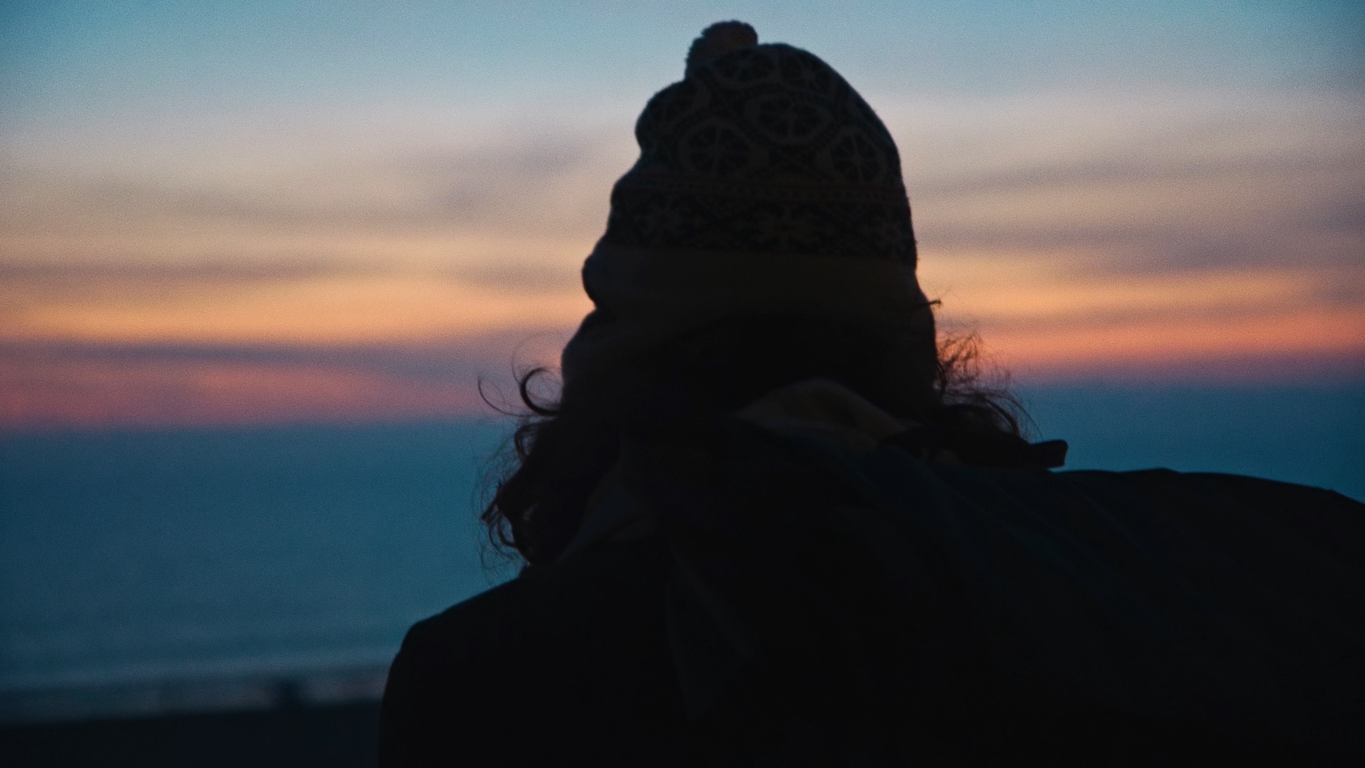 Film still from 'Your Friend Memphis': the silhouette of a person's back, as they look out to a sunset over the ocean.