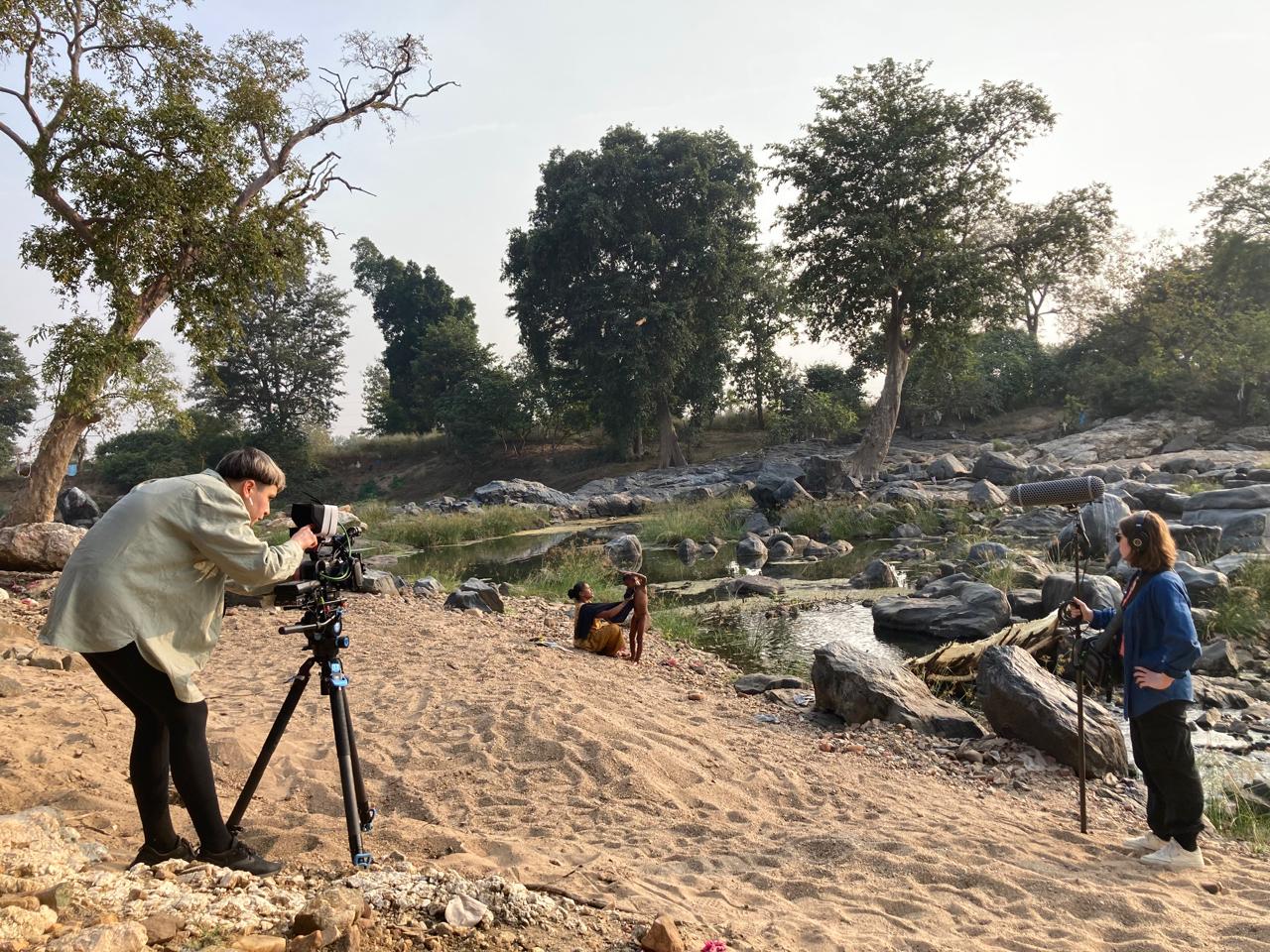 On a sandy beach, two women film a mother and child.