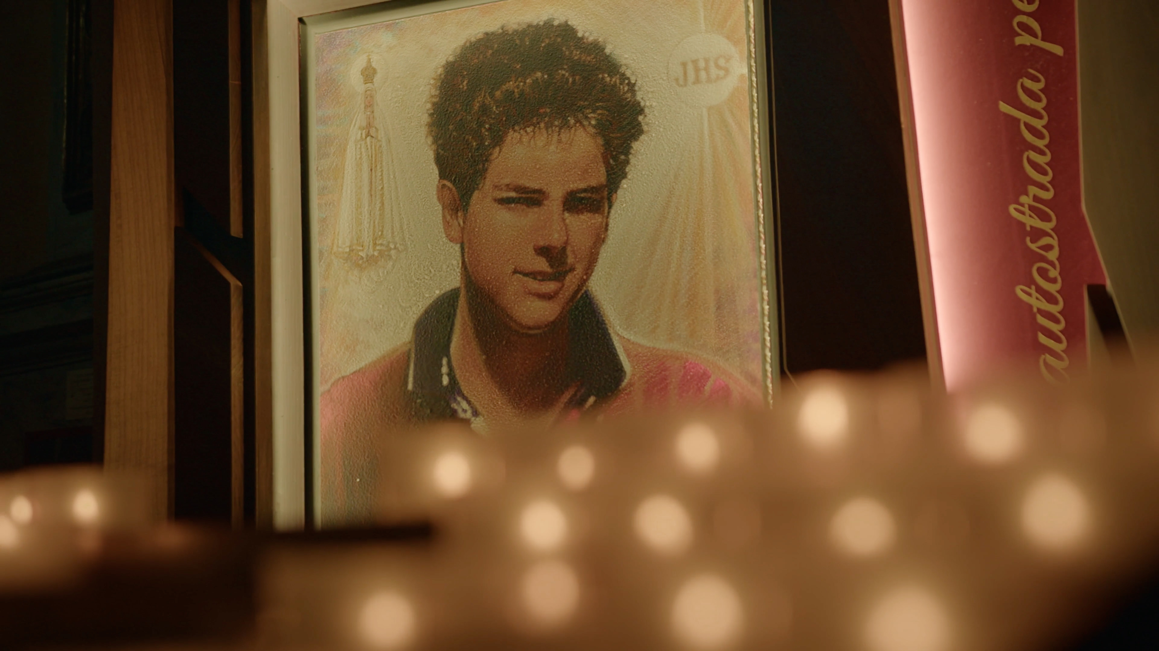With blurry votive candles in the foreground, an image of a photograph of a young man.
