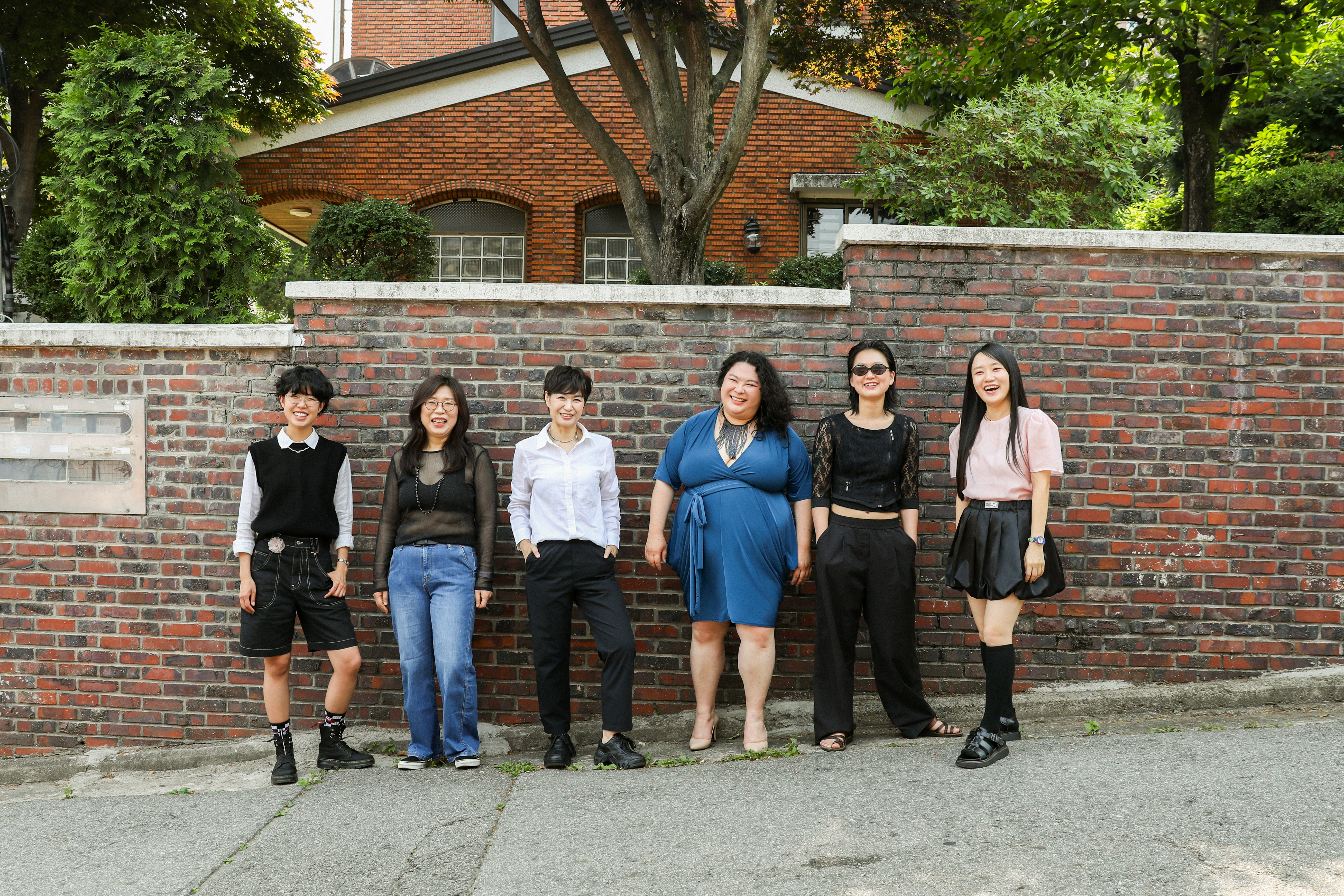 Six women stand against a brick wall.