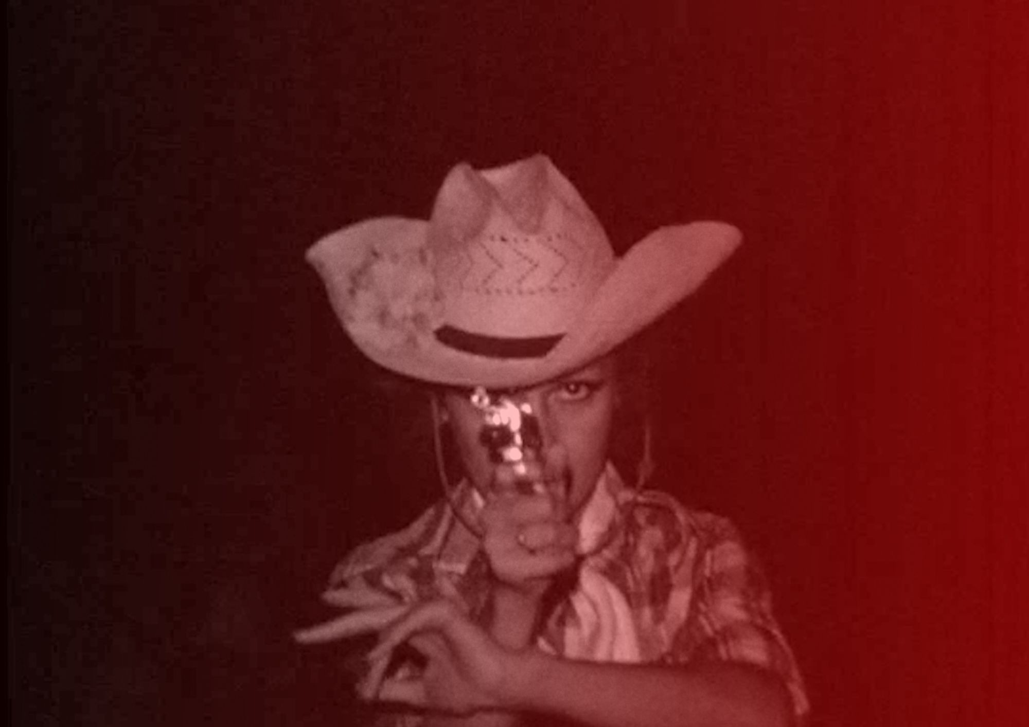 A red-tinted image of a young boy pointing a gun at the camera.