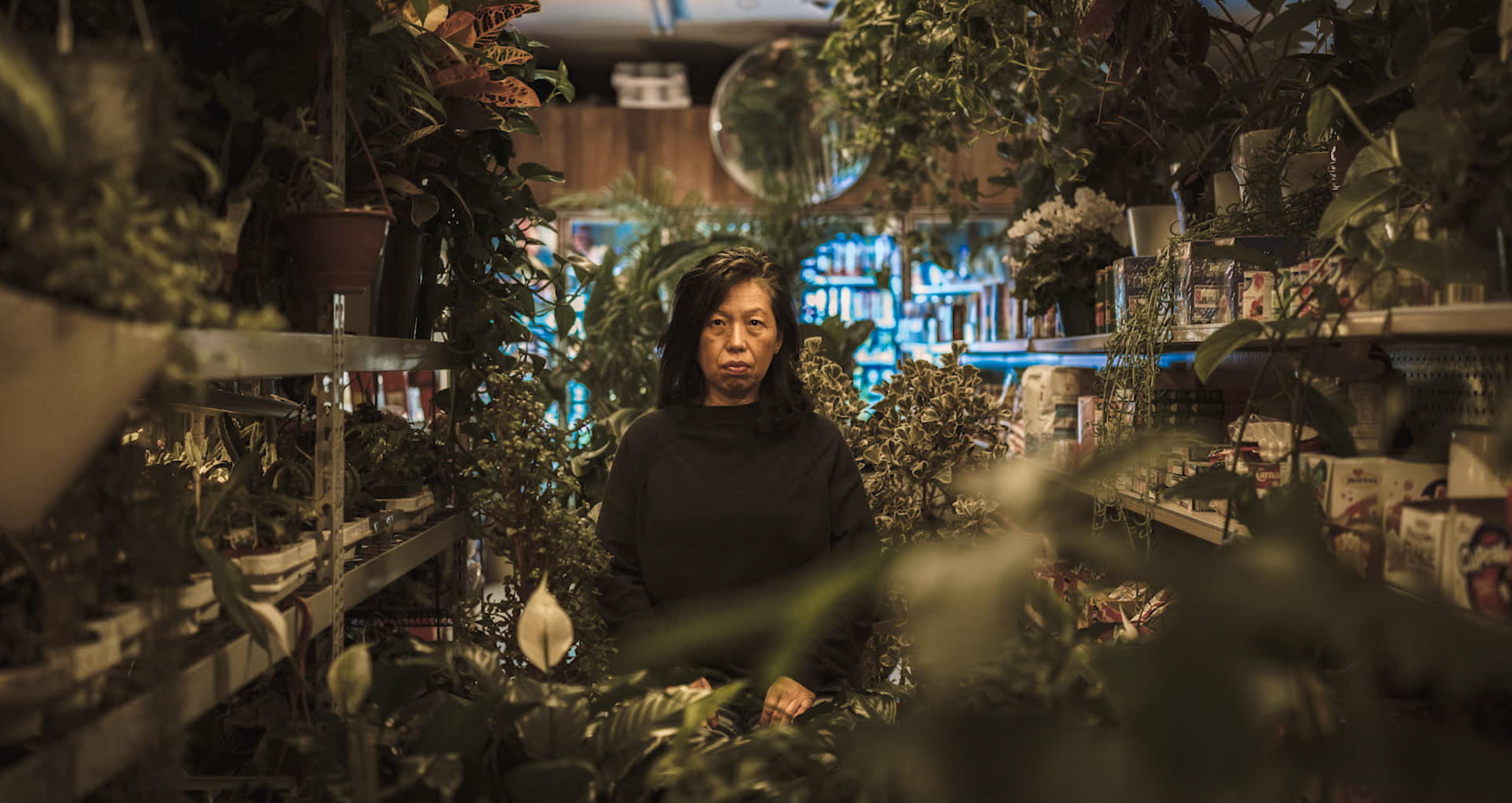 A woman with black hair stands in the middle of a plant shop.