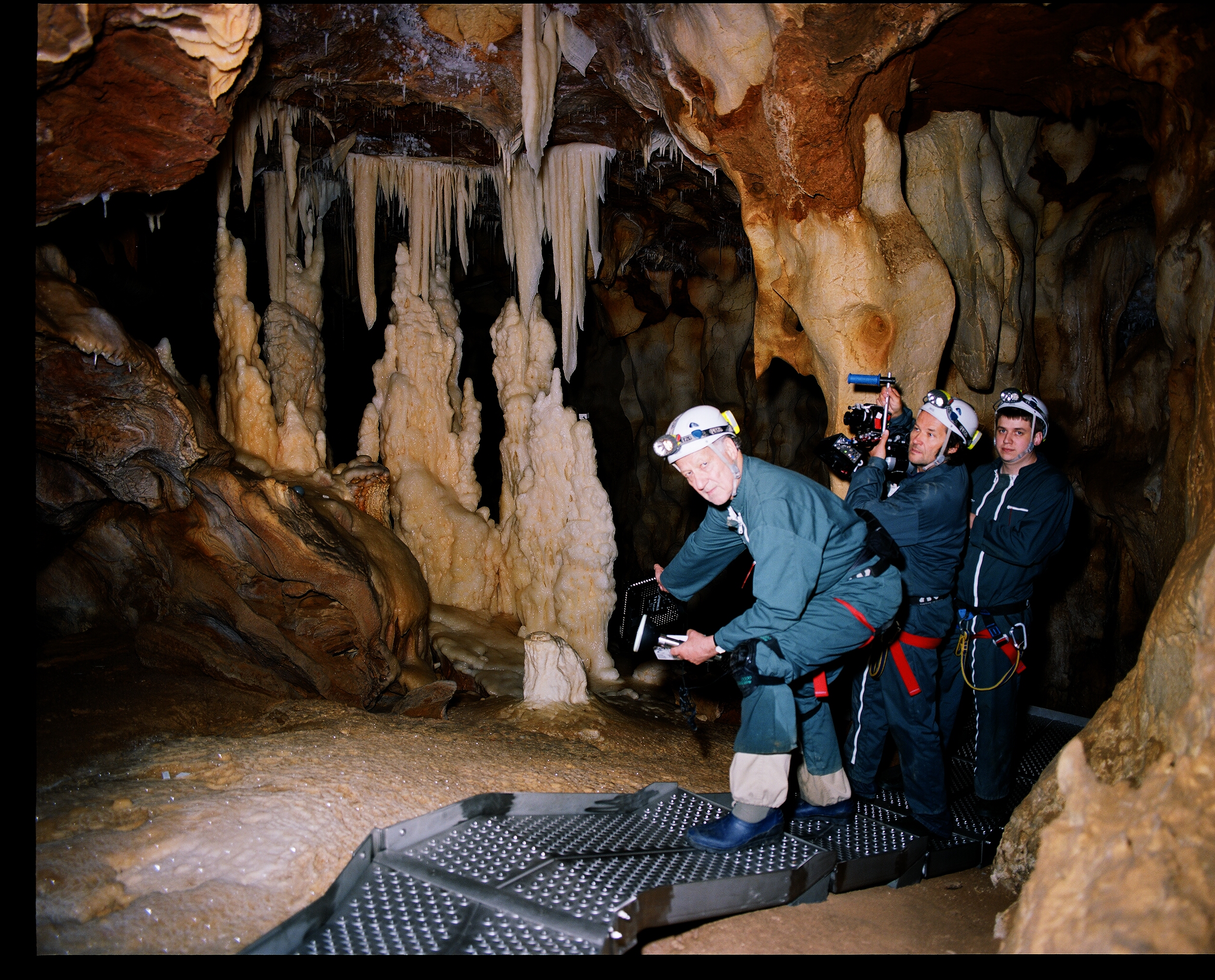 Three middle-aged white men in gear and holding cameras pose for a photo inside a cave lit only by the flash of the camera