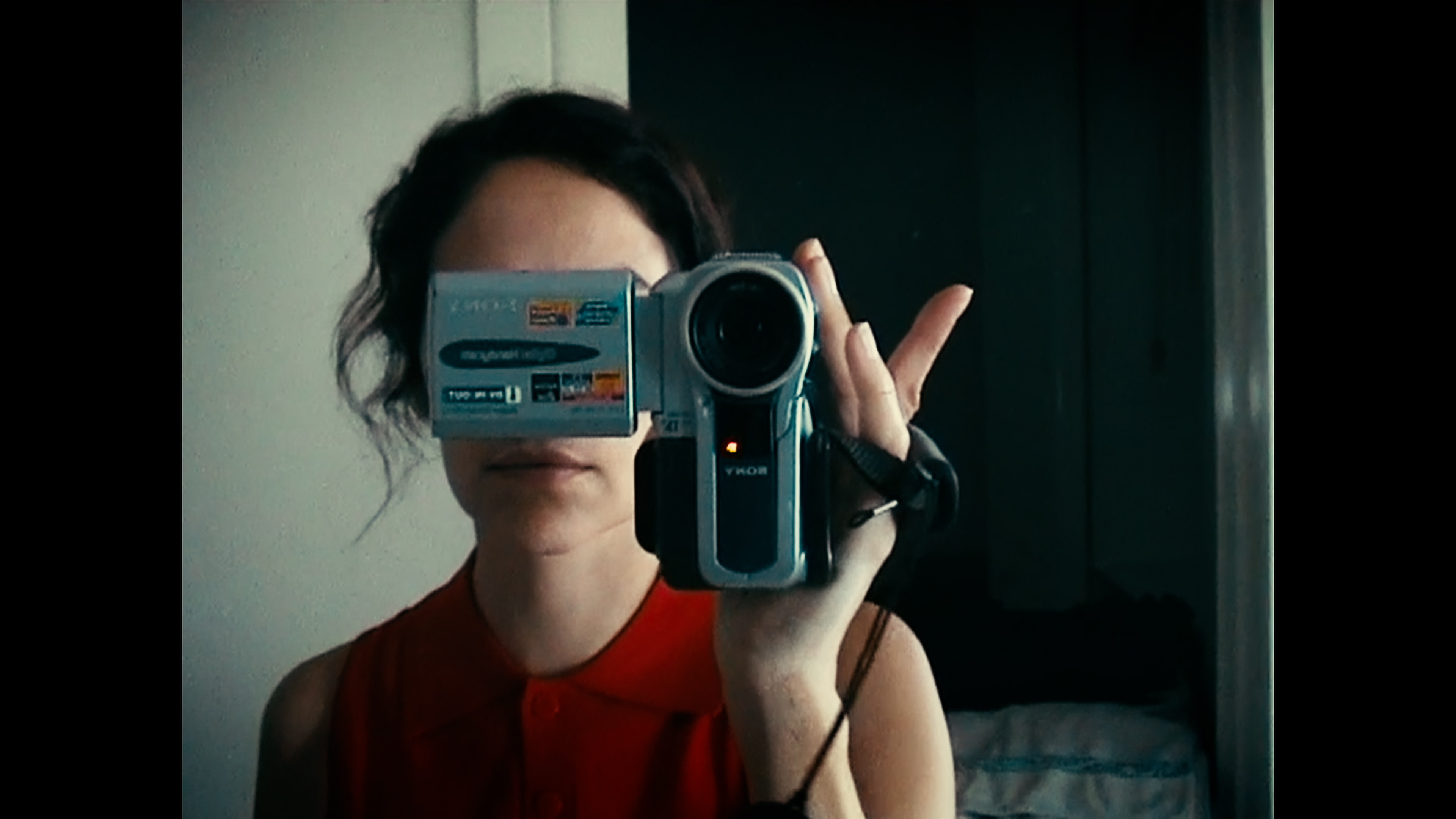 A reflection of a woman in a red, sleeveless top holding a Sony camcorder in front of her face