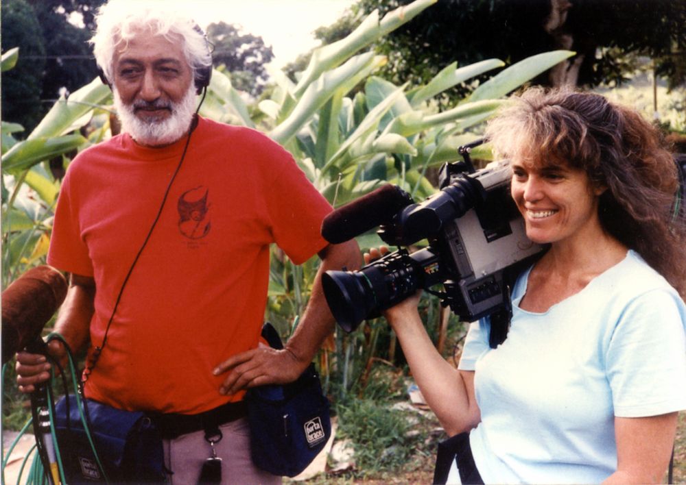 Puhipau, a man holding a mic and wearing headphones, and Joan Lander, a woman holding a camera and smiling, filming in 1989. Courtesy of Joan Lander