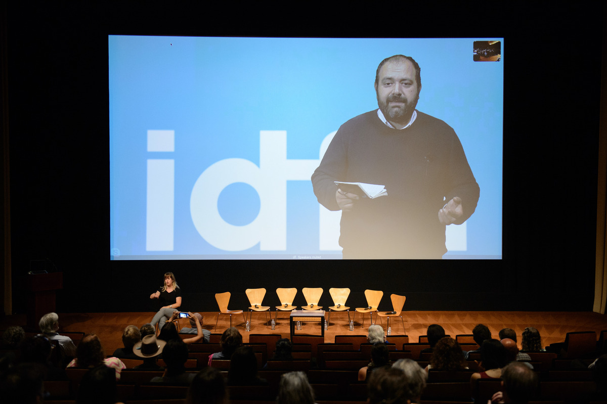 IDFA Artistic Dierctor Orwa Nyrabia, shown delivering a keynote address on a large screen at the 2018 Getting Real conference, is a Syrian man with a beard, wearing a dark sweater. Photo courtesy of AMPAS