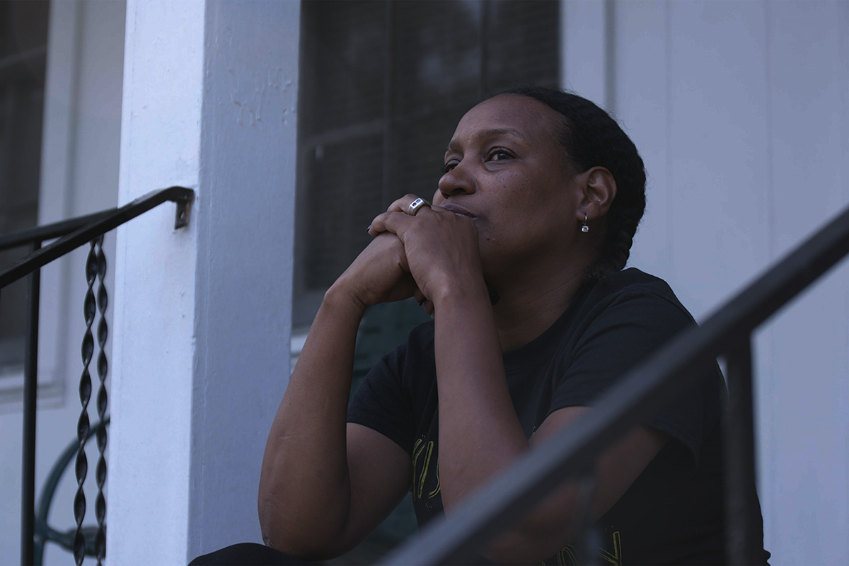Vivian Anderson is a Black woman sitting on a stoop in Columbia, South Carolina, with her hands folded against her chin. She is the founder of EveryBlackGirl, and is seen in Garrett Zevgetis’ ‘On These Grounds.’