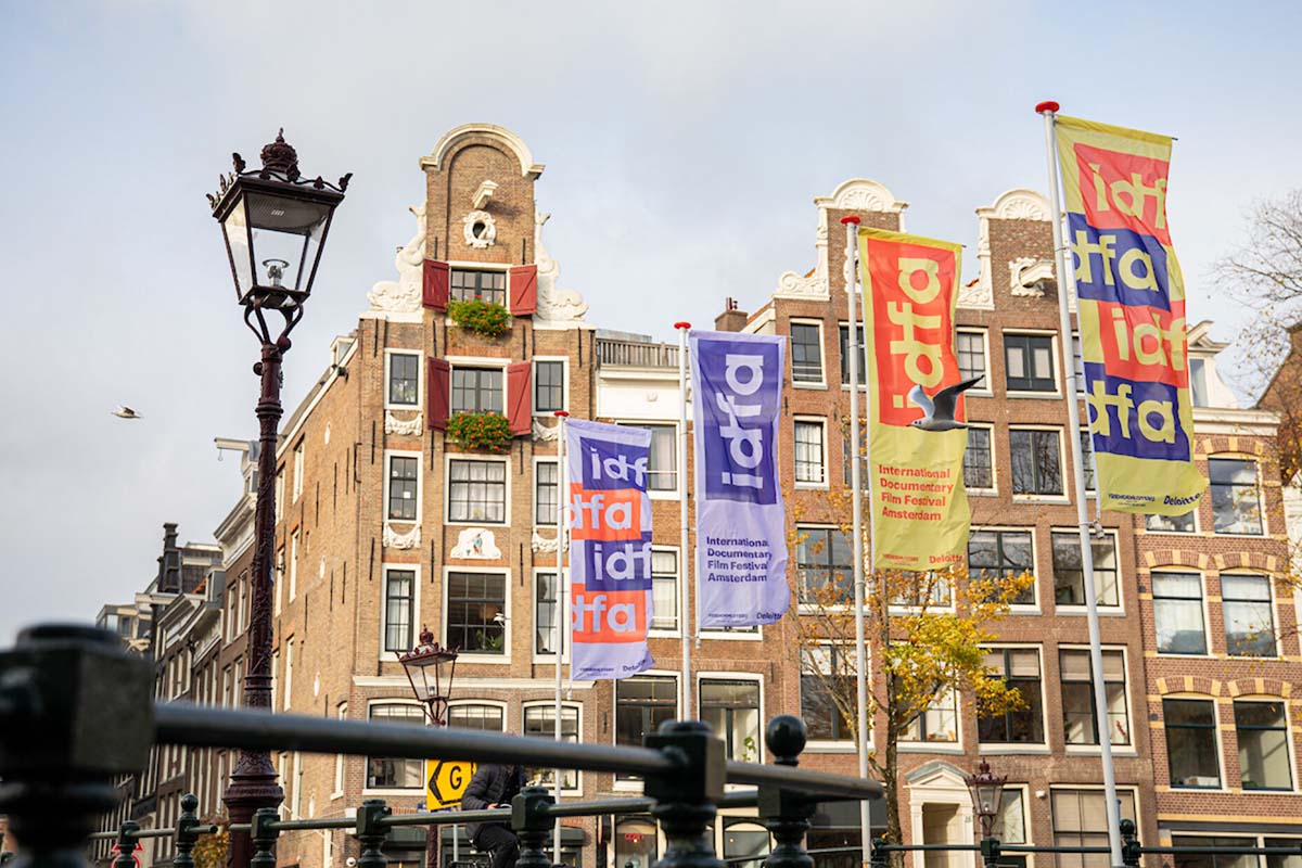 Colorful IDFA 2021 flags fluttering against a brownstone building in Amsterdam. Photo by Roos Trommelen. Courtesy of IDFA.