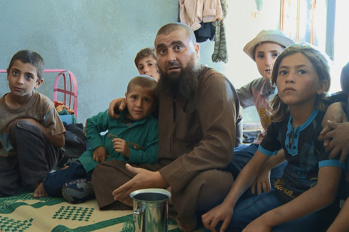 Abu Osama is a bald Syrian man with a beard, sitting with his children at his home in Syria. From Talal Derki’s Academy Award-nominated  ‘Of Fathers and Sons.’ Courtesy of Kino Lorber.