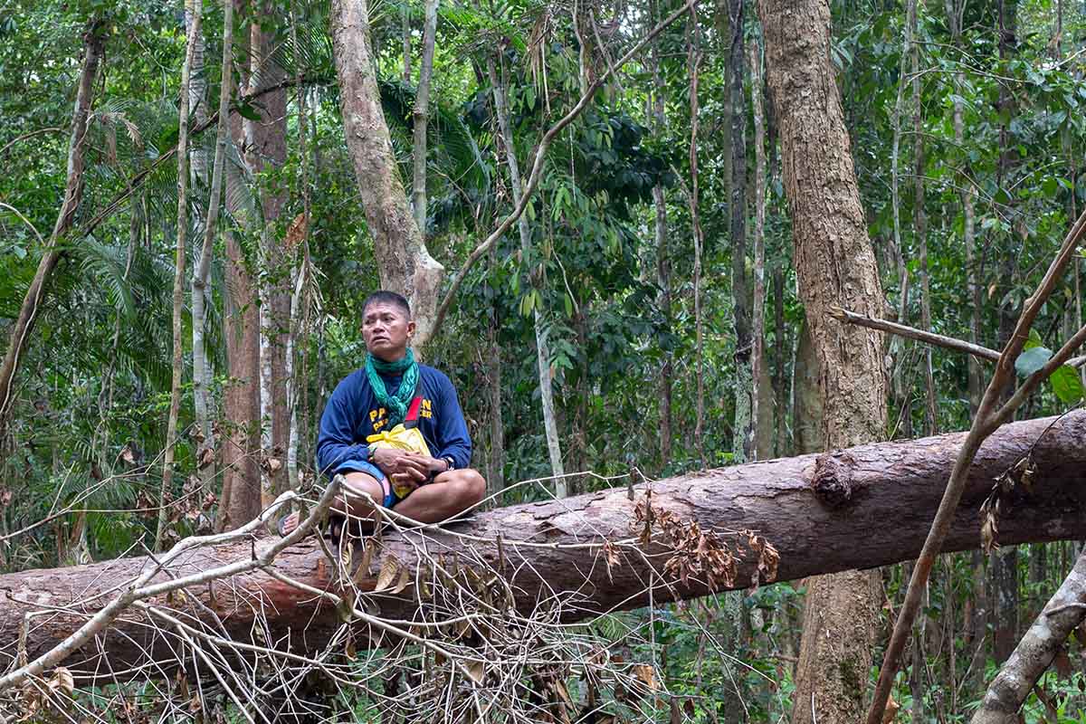 A middle-aged Filipino male activist sits on a fallen tree trunk; he is wearing shorts and a blue t-shirt that says "Palawan para-EnviFORCER." . Photo from Karl Malakunas' 'Delikado.' Courtesy of Hot Docs.