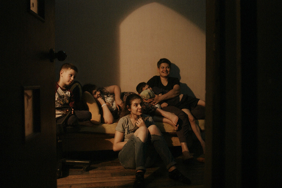 A Ukrainian family of five sits in their living room watching a film that they made about life during wartime. From Iryna Tsilyk’s 'The Earth Is Blue as an Orange'. Courtesy of the filmmaker.