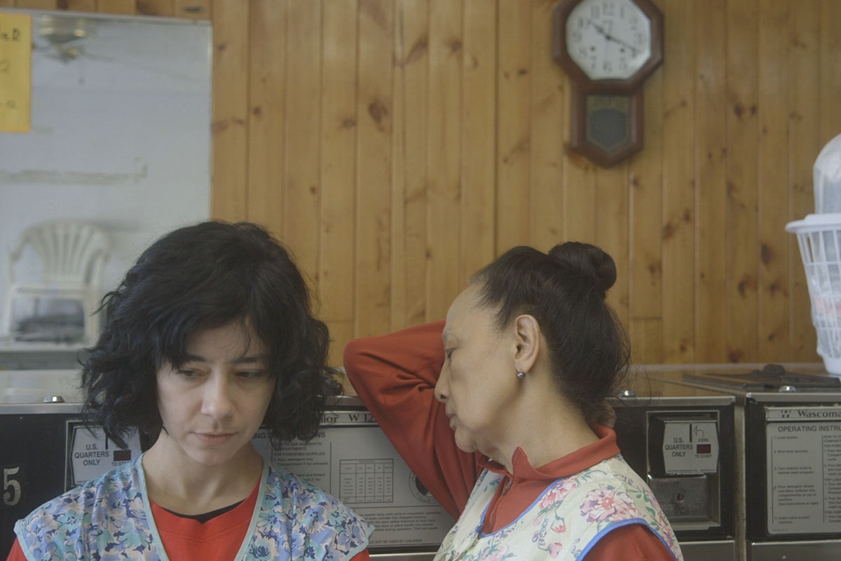 Two female laundry workers are wearing floral aprons and standing against a wooden wall. From Lynne Sachs’ ‘The Washing Society.’ Courtesy of The Criterion Channel. 