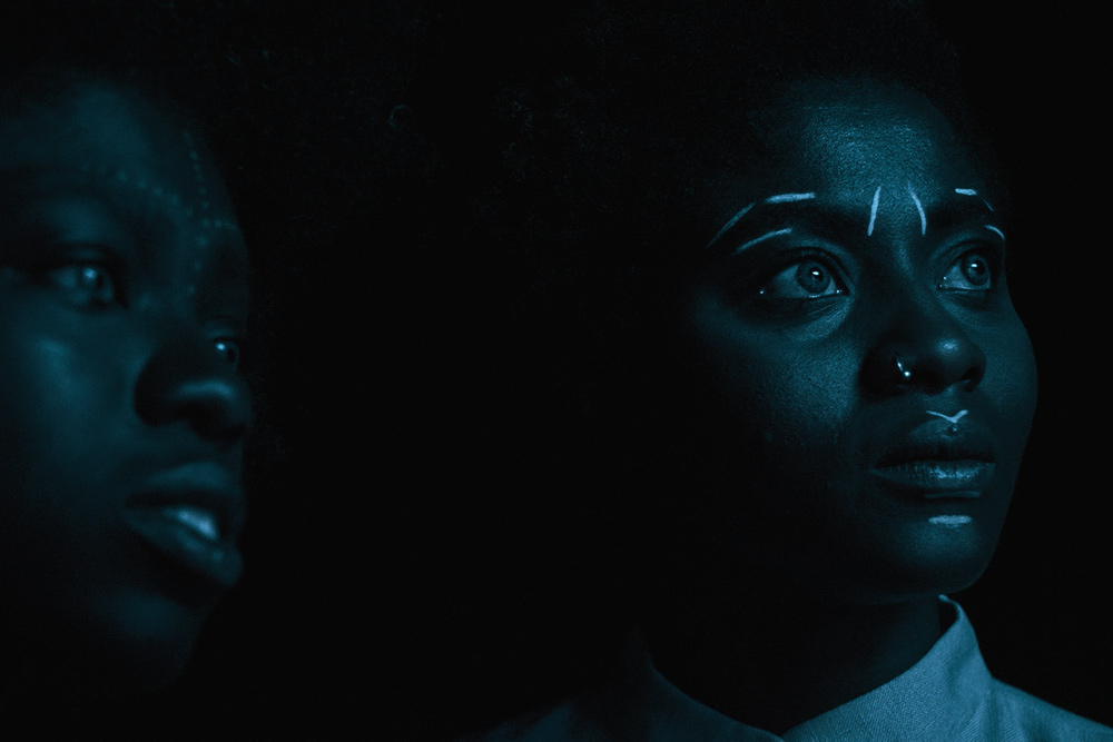 Two young Afro-German women photographed in low light. They have white traditional markings drawn on their faces. Image from Anna Zhukovets’ and Kokutekeleza Musebeni’s ‘Door of Return’. Courtesy of BlackStar Film Festival.