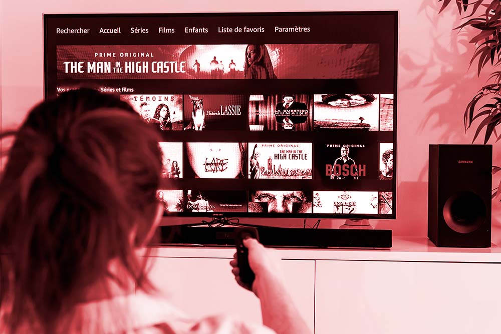 A woman holding a TV remote control facing a screen displaying the homepage of Prime Video.