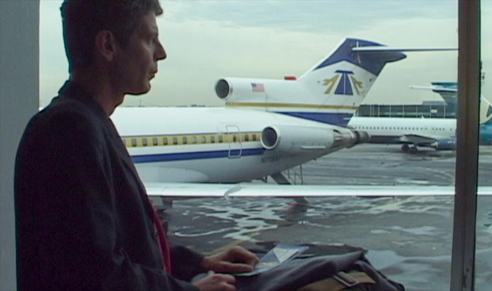 Profile of Anthony Bourdain, a white man in a jacket, against blue and white stationary airplanes. Still from Morgan Neville’s ‘Roadrunner: A Film About Anthony Bourdain.’ Courtesy of Cinetic Media.