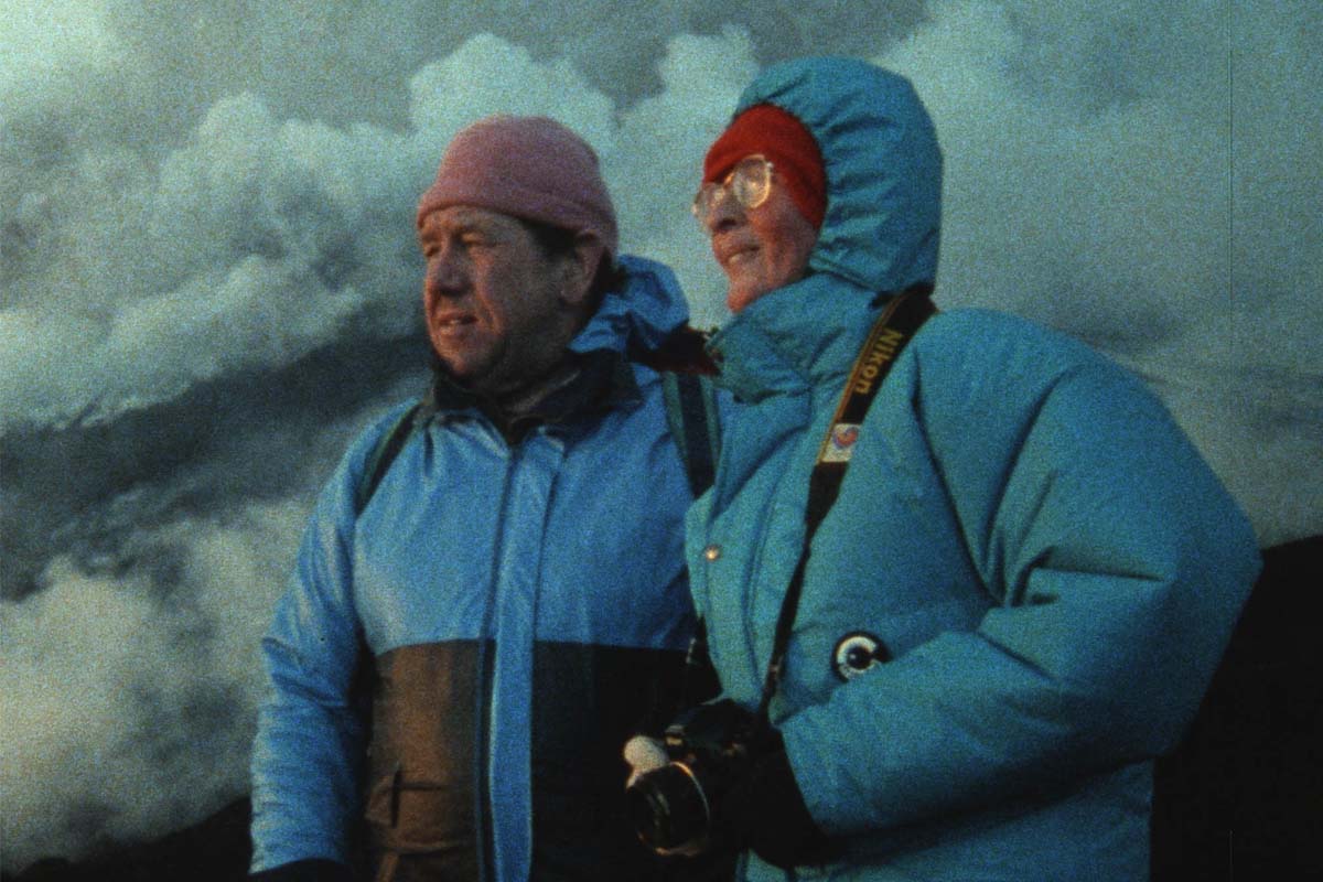 Volcanologists Katia and Maurice Krafft are a white couple seen here wearing blue jackets, against volcanoes emitting smoke. From Sara Dosa’s ‘Fire of Love.’ Courtesy of Sundance Institute.