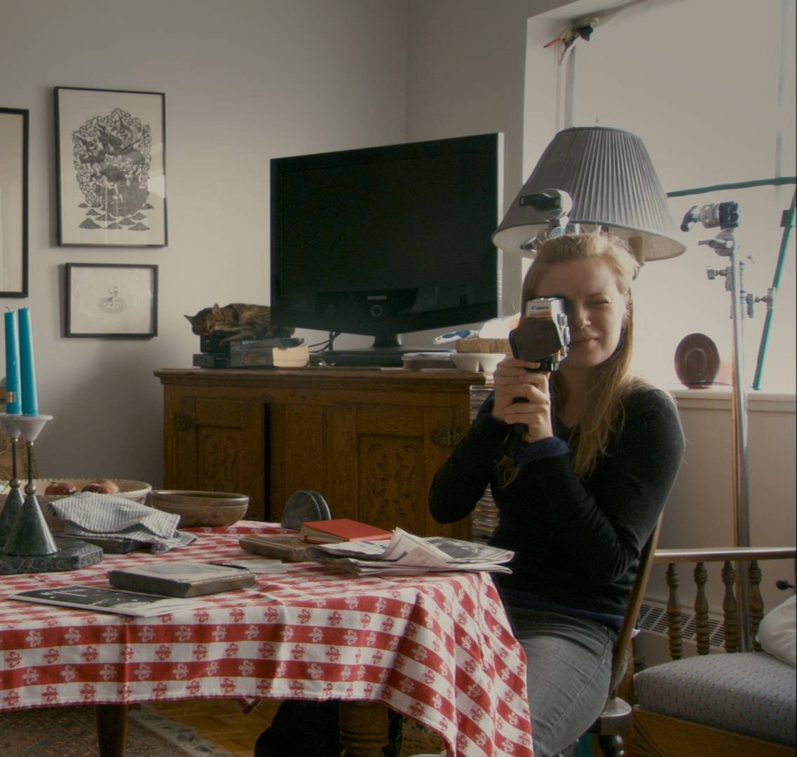 In a living room, Sarah Polley holds a video camera up to her face.