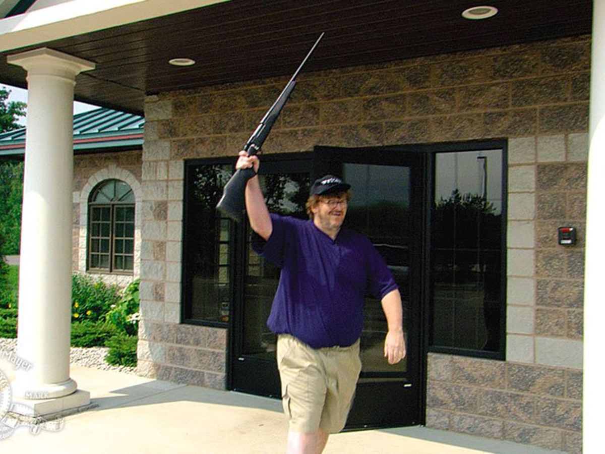 Michael Moore holds aloft a rifle.