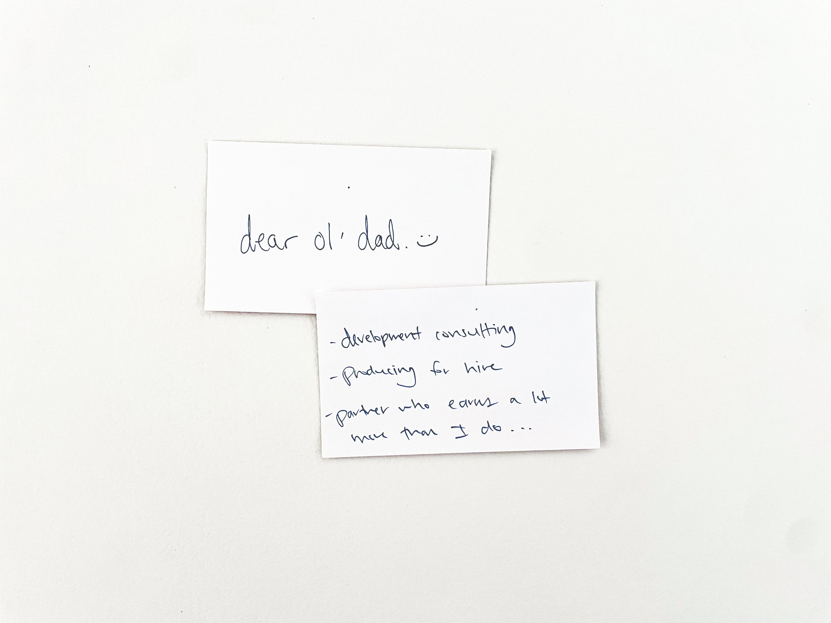 Two white notecards with black writing pinned to a wall. One says 'Dear Ol' dad with a smily face.