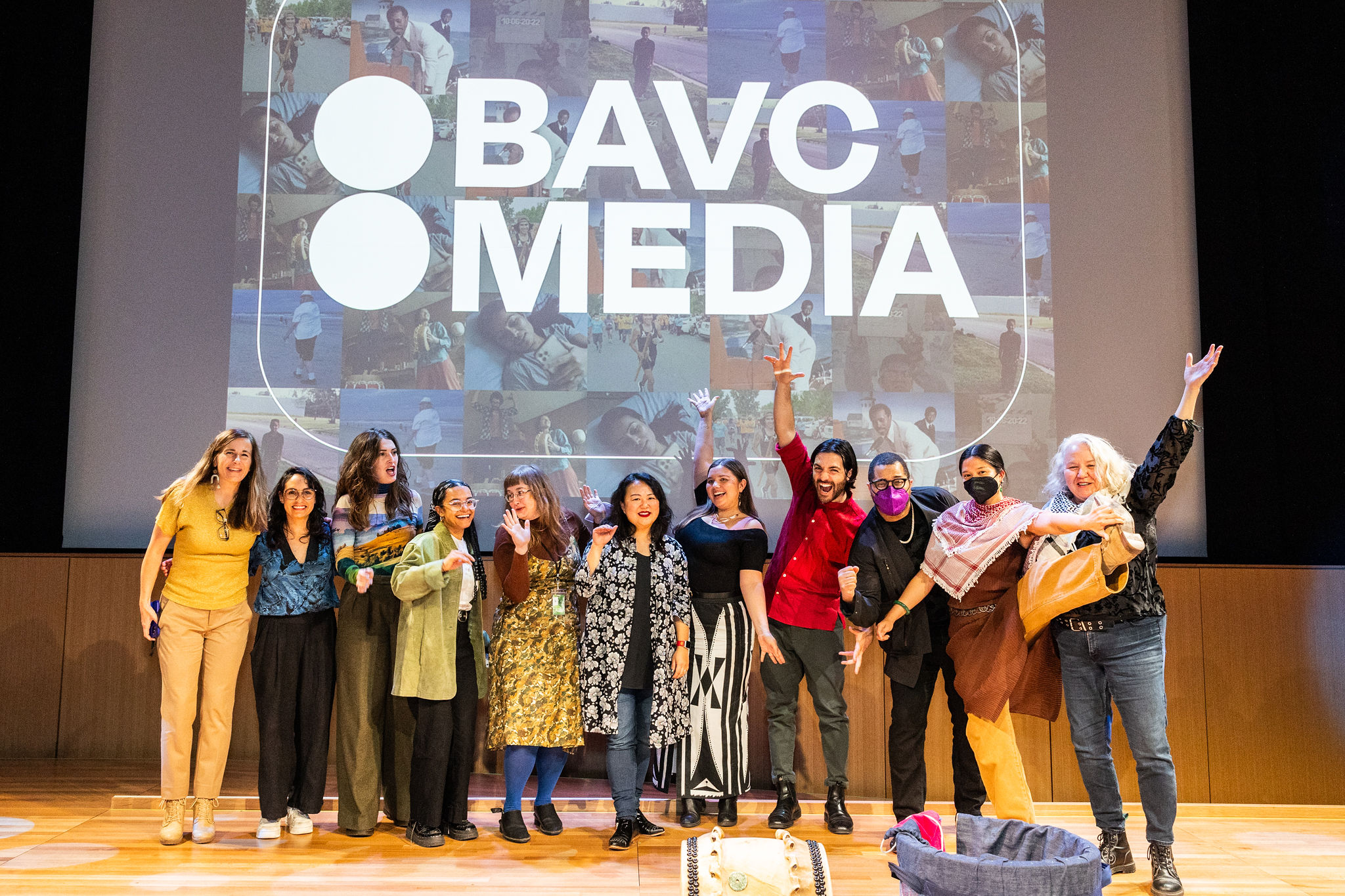 A group of smiling people stand in front of a "BAVC Media" slide projection.