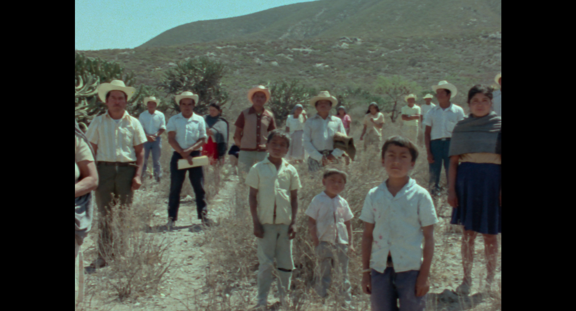 A group of people, including children and adults, stand in on the side of a hill and look at the camera.