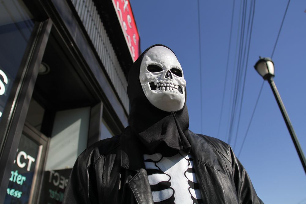 Man in skeleton shirt and leather jacket, wearing a skeleton mask, standing outside