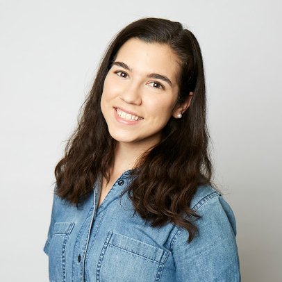 Headshot of a young woman with brown hair wearing a denim button down shirt and pearl earrings