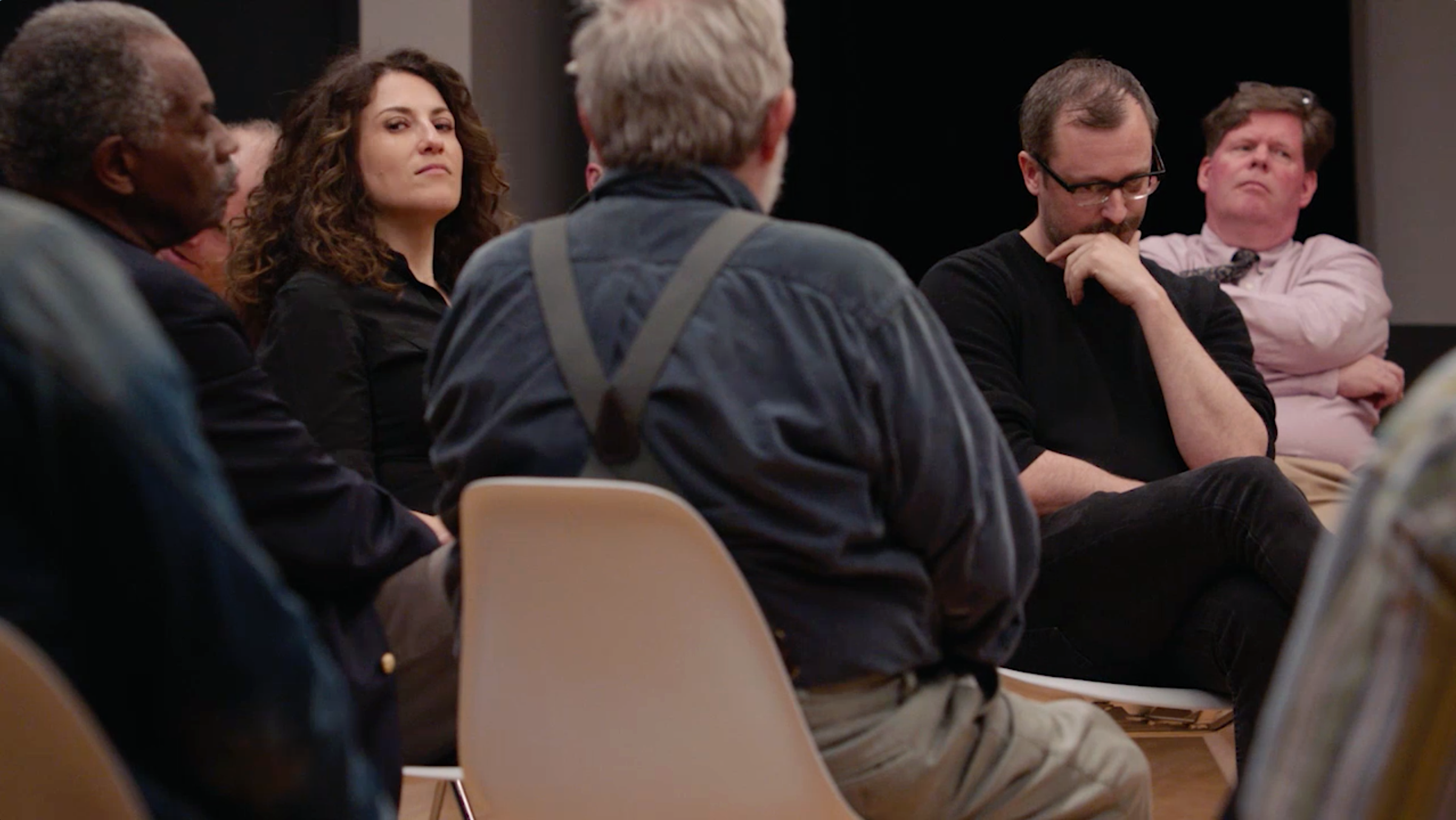 A filmmaker sits in the middle of a circle of hostile onlookers.