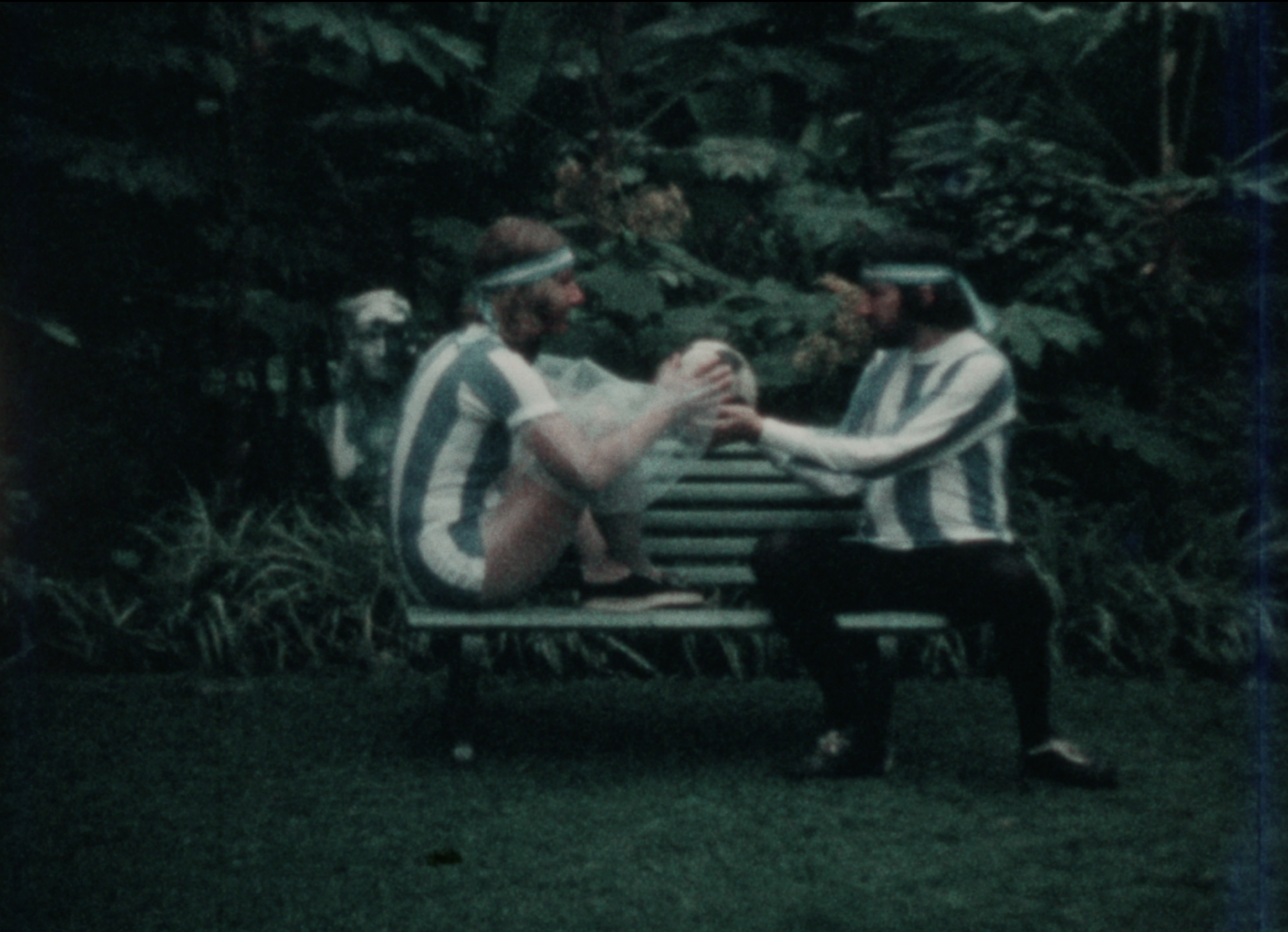 On a park bench, two men in sports jerseys cradle a soccer ball.