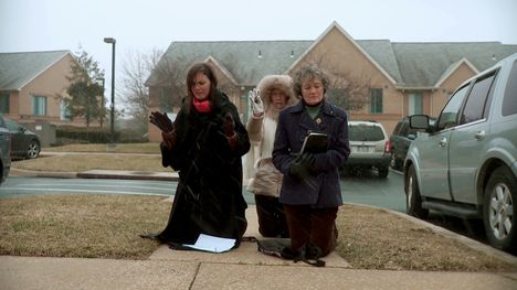 Three middle-aged white women kneeling outside praying