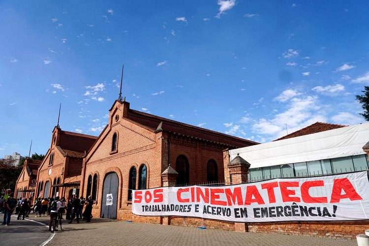 Long shot of the red brick building of Cinemateca Brasileira with a cloth banner that says “SOS Cinemateca.” Photo by Benedito Faga / Alamy Stock Photo.