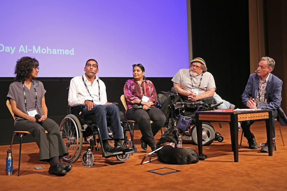 A panel of three men and two women, three in wheelchairs, in converation