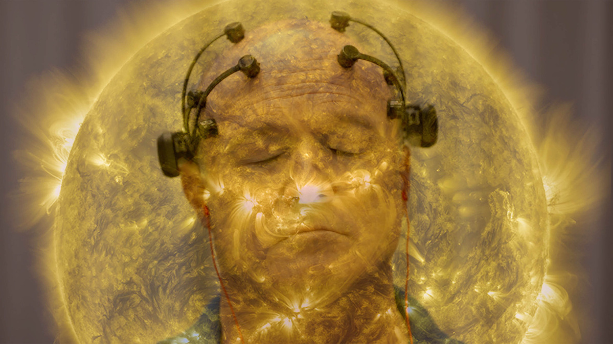 From Theo Anthony, 'All Light, Everywhere.' Courtesy of Sundance Institute. A man, who is particiapting in a neuroscience focus group, has his eyes closed, and is wearing a device on his head comprised of four neurosensors attached to the top of his head and twolarger sensors above each ear. He in enveloped in a golden aura that resembles the sun.