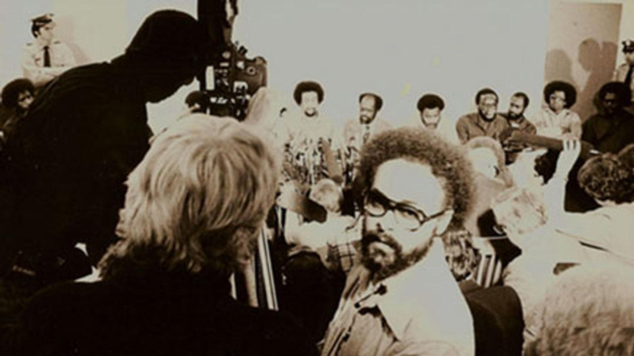 Haile Gerima is a Black filmmaker with short curly hair and a beard. He is seen filming ‘Wilmington 10, U.S.A – 10,000’ (1979). Image courtesy of The Academy Museum of Motion Pictures.