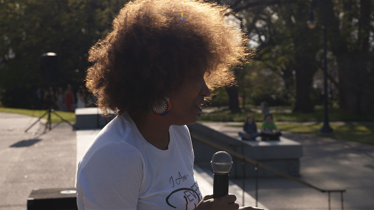 Vivian Anderson, a Black woman with short, brown curly hair and wearing a white shirt,  addresses a crowd at the South Carolina State House . From Garrett Zevgetis’ ‘On These Grounds.’