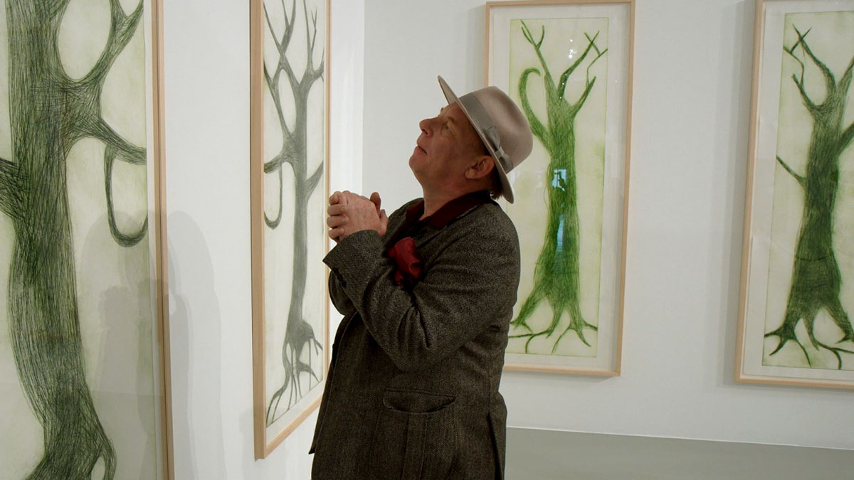 Ben Becker is a white, German actor, wearing a suit and staring at framed art, imitating artist Albert Oehlen. From Oliver Hirschbiegel’s ‘The Painter.’ Courtesy of Picture Tree International.