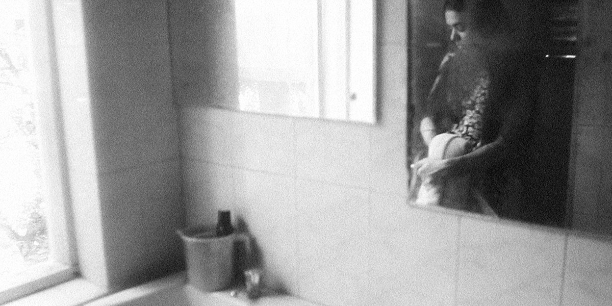 Black-and-white image of a young South Asian woman’s reflection on a bathroom mirror. From Payal Kapadia’s ‘A Night of Knowing Nothing.’ Courtesy of TIFF