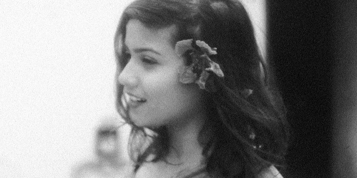 Black-and-white image of a young, smiling South Asian woman with a flower in her hair. From Payal Kapadia’s ‘A Night of Knowing Nothing.’ Courtesy of TIFF