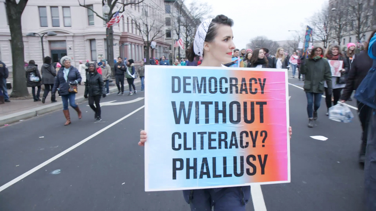 From Maria Finitzo's 'The Dilemma of Desire.' In this image, a woman is particpating in a demonstration on a city street; she carries a sign that reads "Democracy without cliteracy? Phallusy." Courtesy of Kartemquin Films