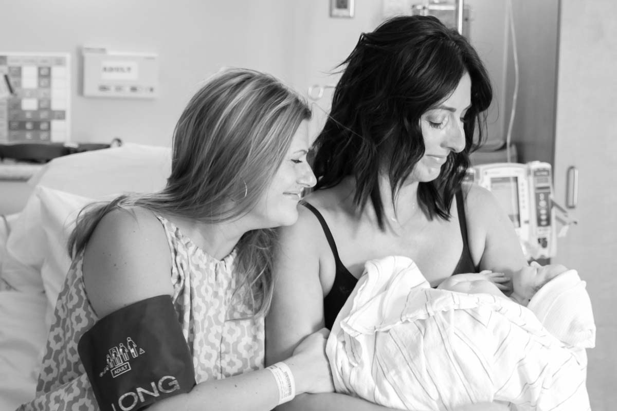 Two white woman, one, a surrogate, the other, a new mother, sit on a hospital bed with a newborn baby. Courtesy of PBS.