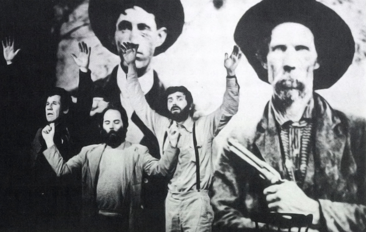 Three men have their arms raised with a scene of two cowboys projected behind them. From Roadside Theatre's performance of Red Fox/Second Hangin' 