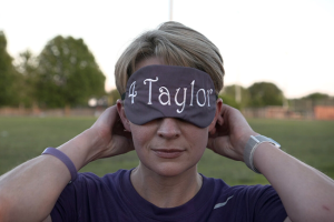 Close up of a woman with short, blonde hair wearing a blindfold that reads "4 Taylor"