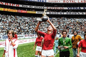 Film still from 'Copa 71'. Woman soccer player holding up World Cup trophy in a stadium filled with fans and her team on the field with her.
