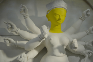 A white clay figure of a Hindu goddess with a face that is painted yellow.