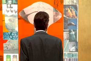 The back of a man in a suit as he stands in front of colorful artwork