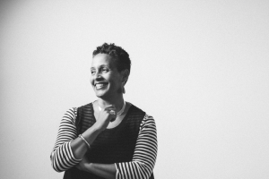 A black and white photograph of a smiling Black woman with short hair. She is wearing a dress with striped sleeves.