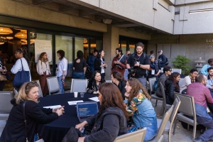 Outside in a courtyard, groups of filmmakers sit around circular tables.