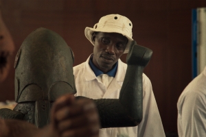 A Black man in a white jacket looks at a statue.